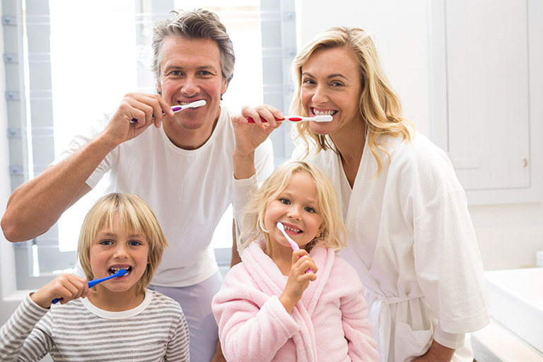 A happy family of four all brushing their teeth together