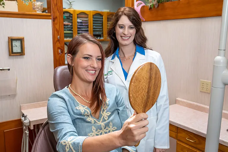 Image of Dr. Luscri and a patient in a cosmetic dentistry consultation, where the patient is holding a mirror and looking at her smile.