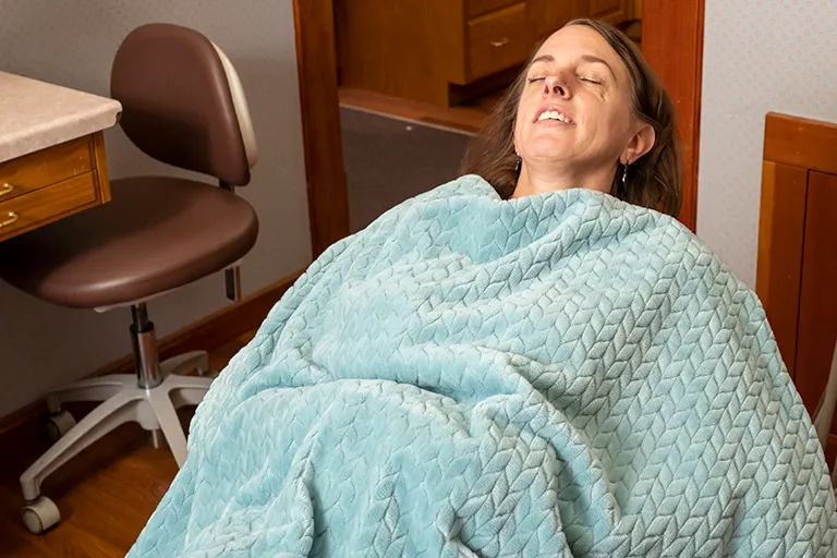 Image of a person laying in a dental chair with a cozy blanket.