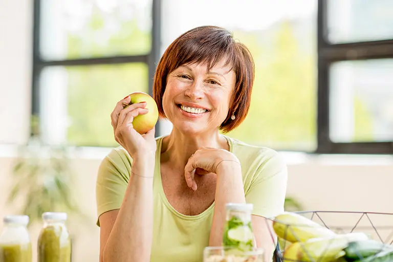 Image of a person holding an apple and smiling at the camera.